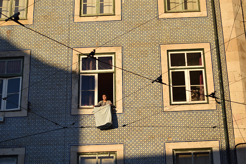 a woman hanging her laundry out her window in Lisbon Portugal