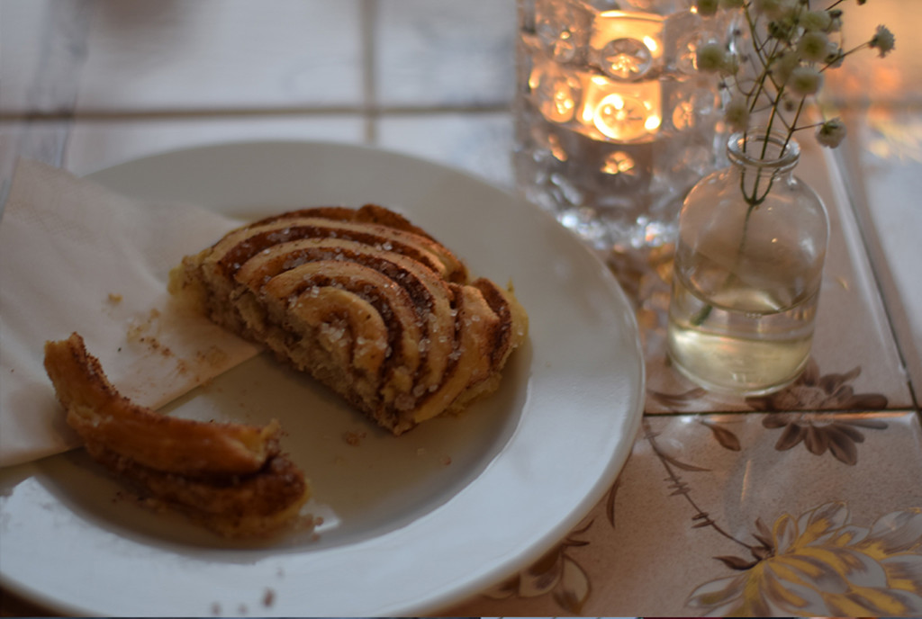 Photo of a cinnamon roll on a plate next to a candle in the Krog og Krinkel Bokcafe in Bergen, Norway.