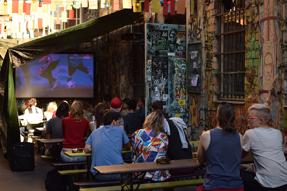 photo of a group of people watching a soccer game on a screen at a Berlin cafe.