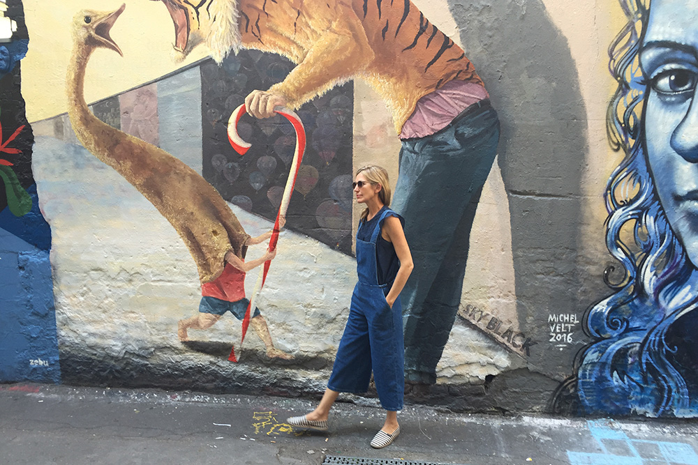 Photo of a woman standing in front of a wall of street art in Berlin.