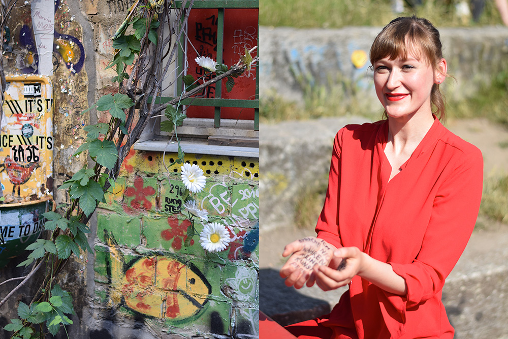 A photo of a wall filled with street art and a photo of a young woman who is smiling and holding out her hands which have writing on them. Berlin, Germany.