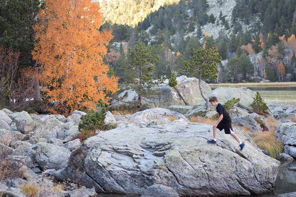 Photo of a boy walking across large stones in near a lake in the Spanish Pyrenees.