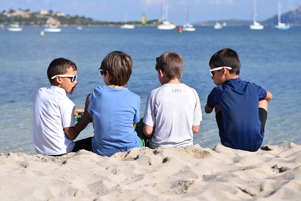 A photo of 4 boys sitting on a white sandy beach together in Mallorca, Spain.