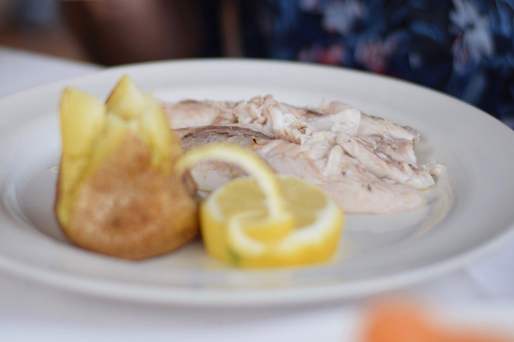 Photo of a dinner table with a plate of fresh grilled fish, a potato and a lemon in Ravello, Italy.