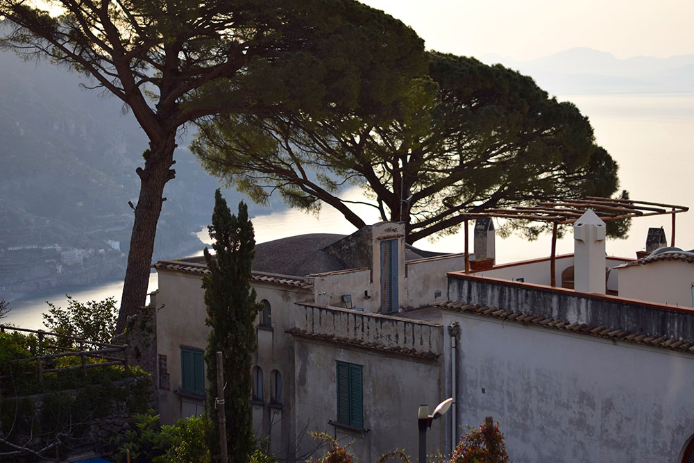 Photo of a beautiful old building surrounded by trees and the Mediterranean Sea in the background in Ravello, Italy.