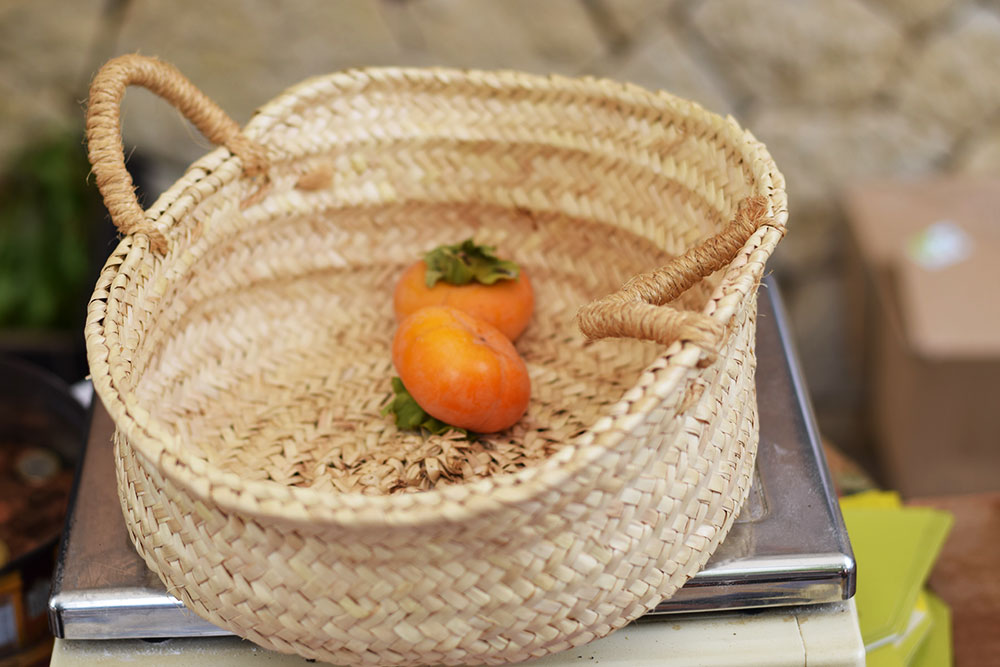 Photograph of two ripe persimmon fruits in a basket at the Santa Maria market in Mallorca, Spain.