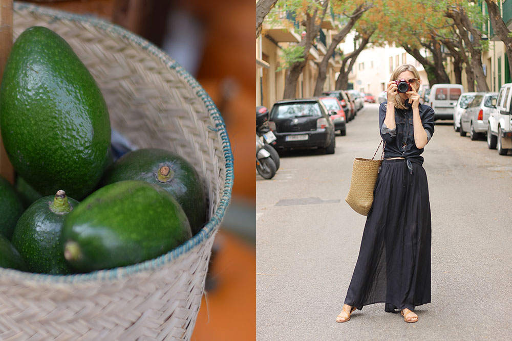 Photograph of a basket of avocados and a woman taking a photograph on a small street near the Santa Maria market in Mallorca, Spain.