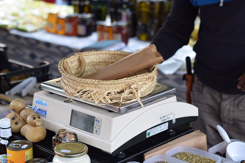 Photograph of a man weighing items in a basket at his table at the Santa Maria market in Mallorca, Spain.