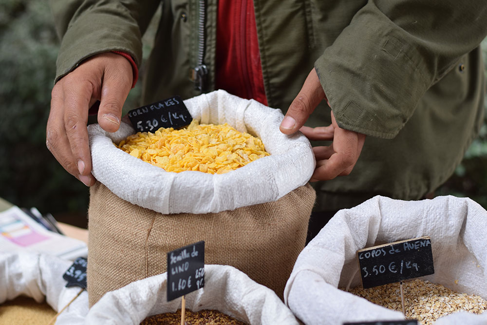 Photograph of a seller holding a burlap bag of bulk cereal at the Santa Maria market in Mallorca, Spain.