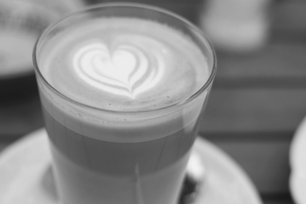 A black and white photo of a cup of coffee with a heart shaped milk foam design.