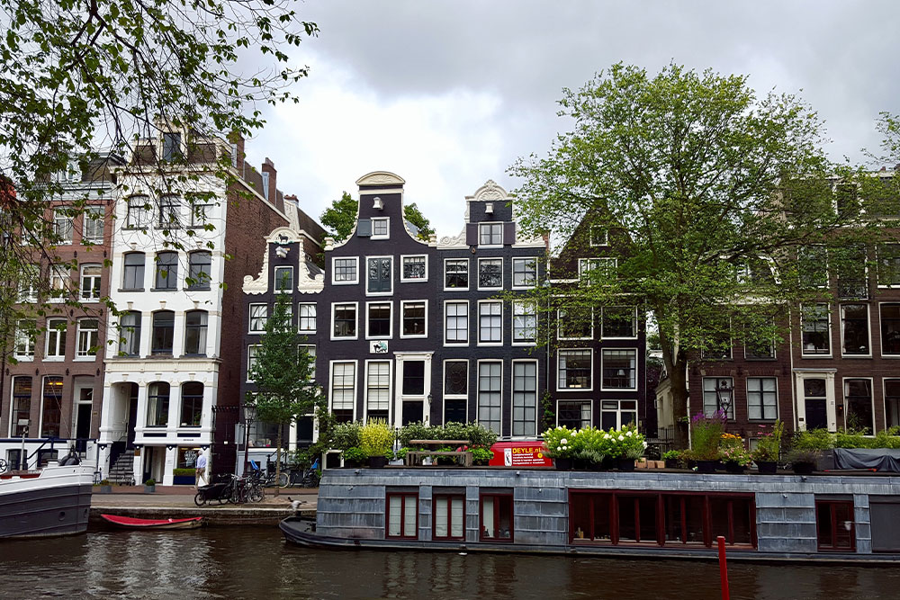 A photo of a row of houses along a canal in Amsterdam with a large houseboat and a few smaller boats in front. 