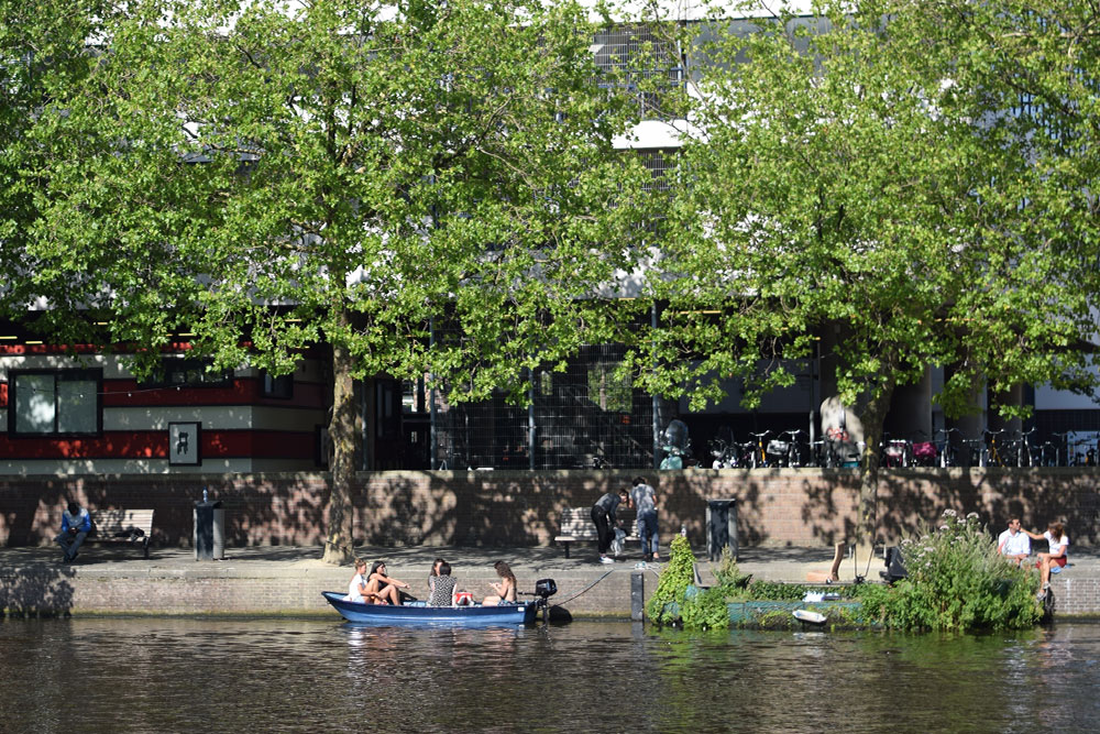 A photo of a boat filled with friends sitting in the summer sun in a canal in Amsterdam.