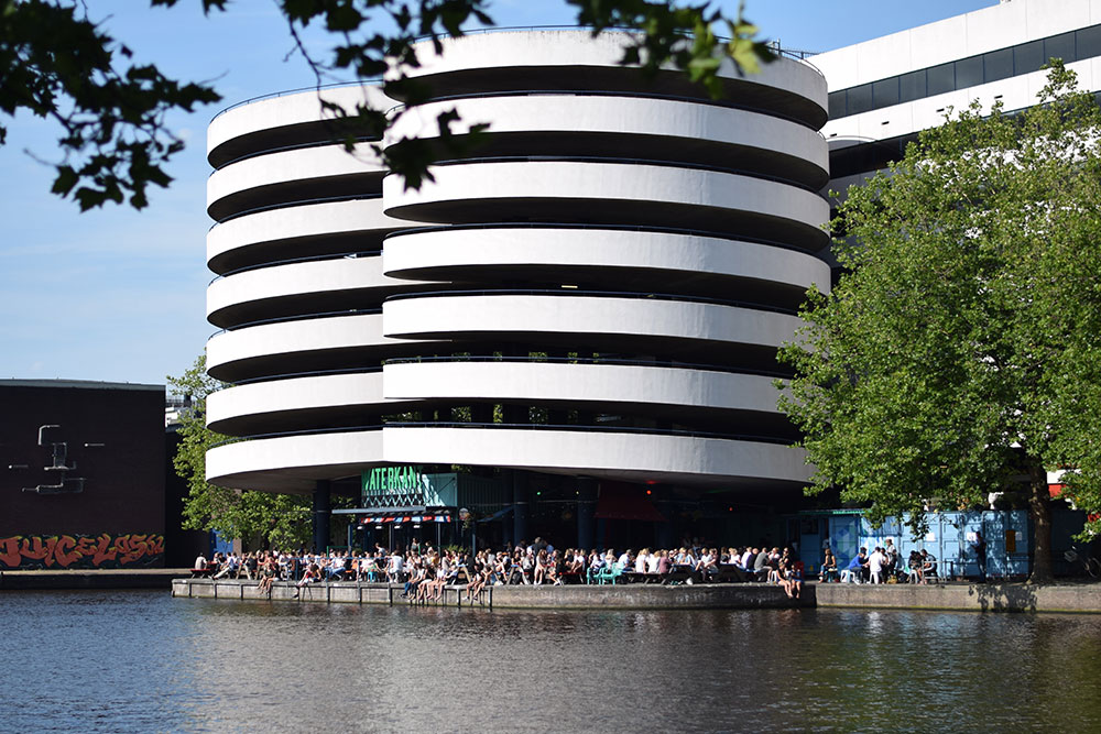 A photo of Waterkant restaurant in Amsterdam with a patio full of people enjoying food and drinks in the sunshine.