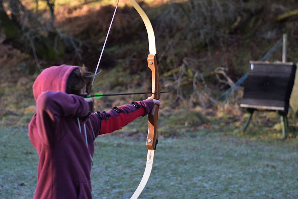 Photo of a boy shooting an arrow with a bow.