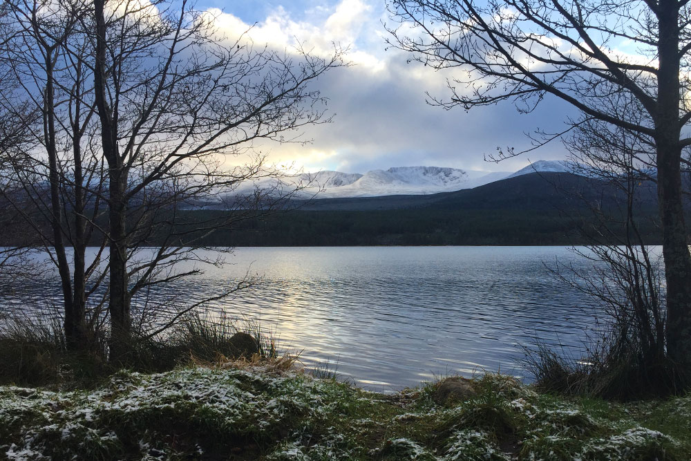 Photo of a loch in the Scottish Highlands with snowy mountains in the distance.