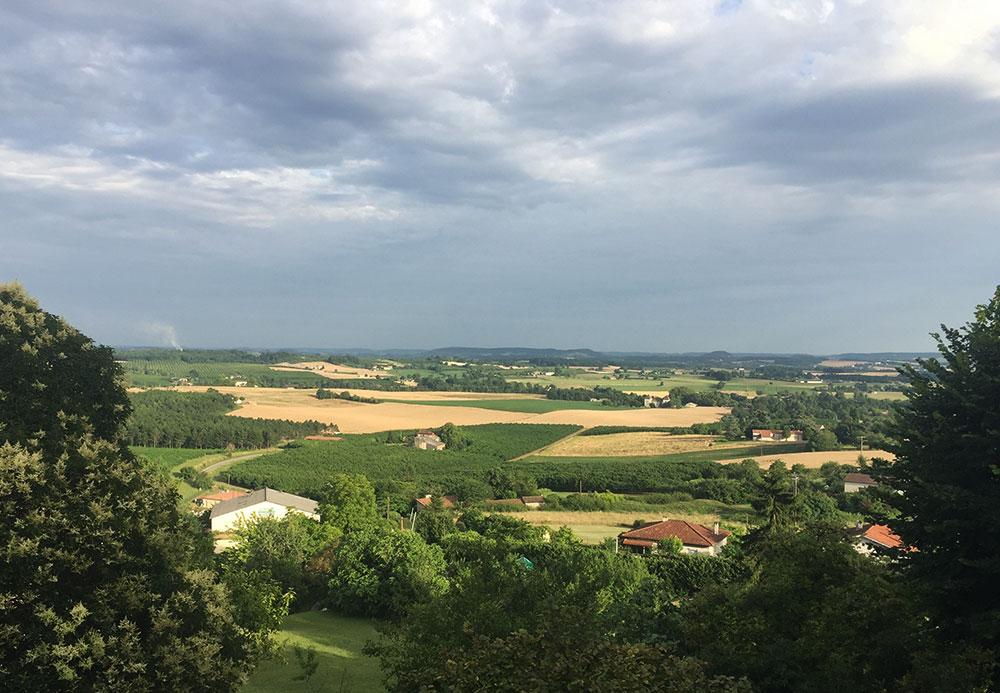 A long view of the Dordogne river valley with wheat colored patches, green patches, trees and sky.